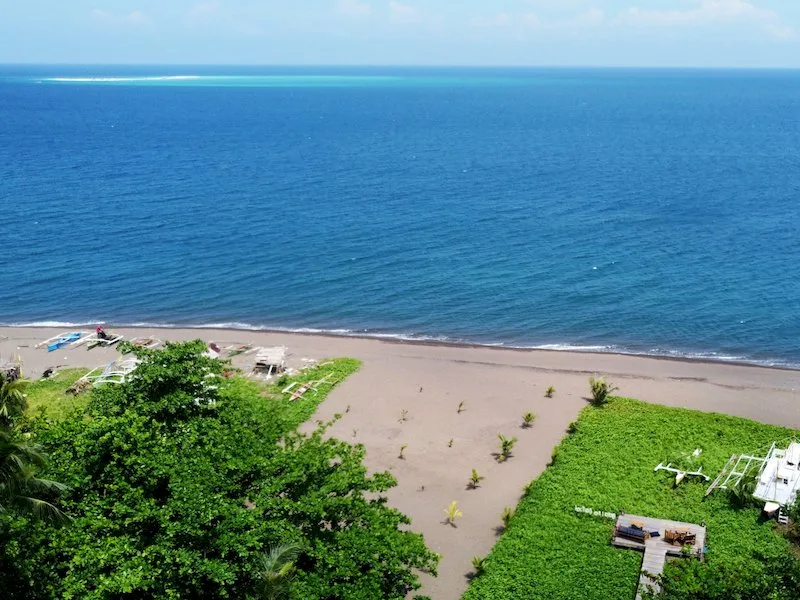 Plage de sable, mer bleue, bateaux à quai et végétation luxuriante