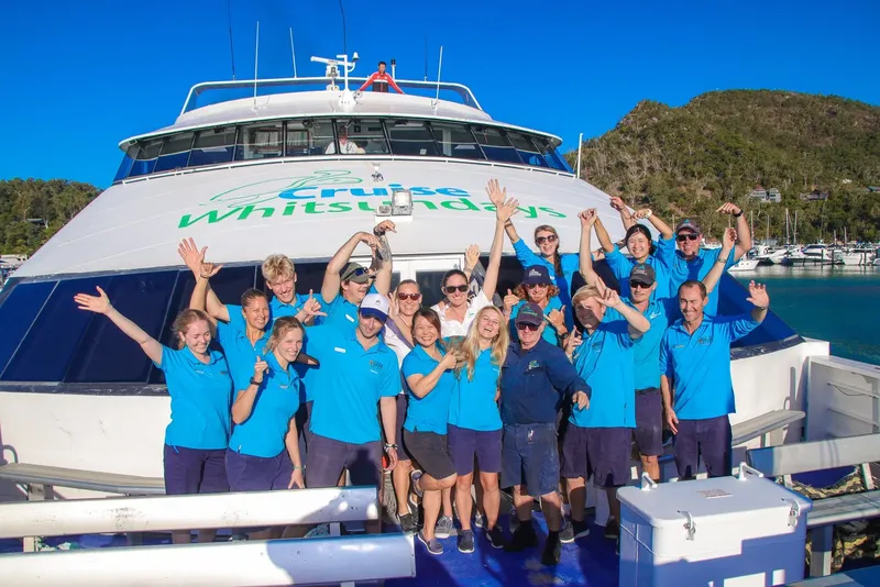 Equipe souriante devant un grand bateau de croisière bleu et blanc