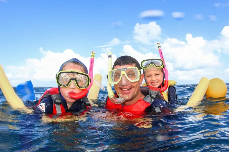 Trois personnes sourient avec masque et tuba dans l'eau