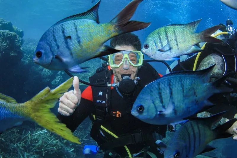 Plongeur souriant avec pouce levé entouré de poissons tropicaux colorés