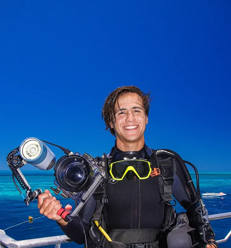 Plongeur souriant avec appareil photo, combinaison et masque, ciel bleu