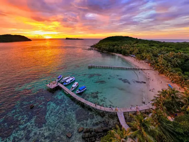 Plage tropicale avec ponton, bateaux et quelques personnes au coucher du soleil