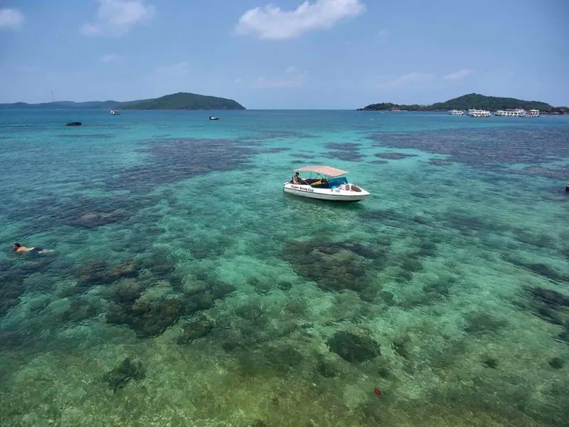 Bateau de plaisance navigue sur une eau turquoise peu profonde avec des nageurs