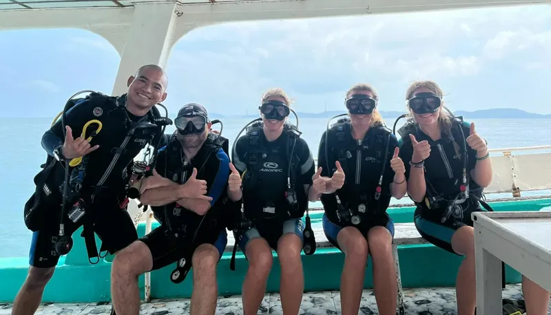 Cinq plongeurs souriants avec leur équipement sur un bateau