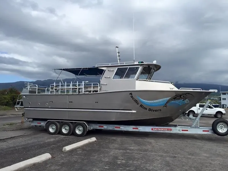 Bateau de plongée gris sur remorque, ciel nuageux, parking visible