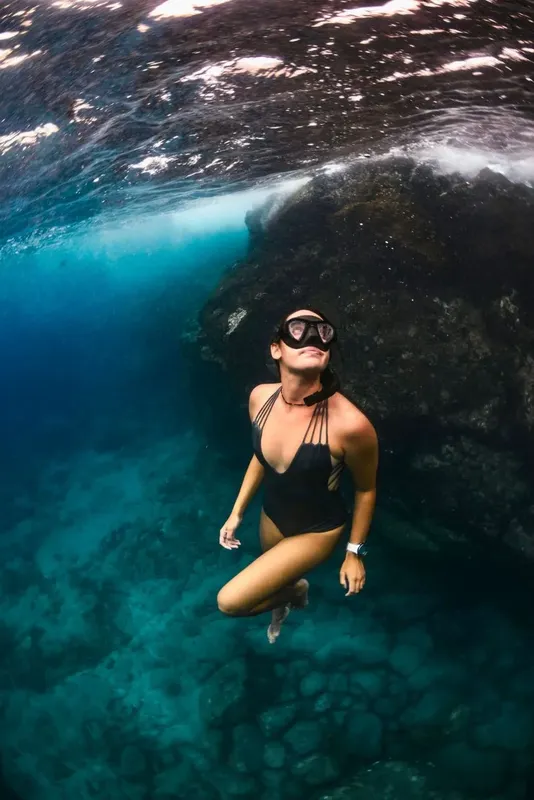 Femme en maillot de bain nageant en apnée dans une eau turquoise claire