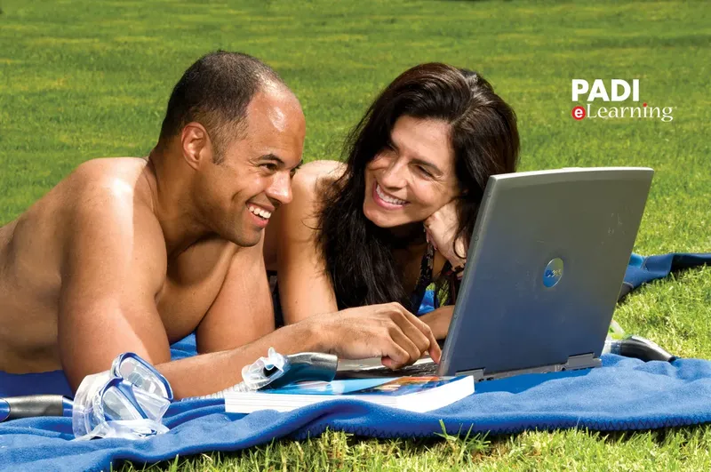 Couple souriant regardant un ordinateur portable avec du matériel de plongée