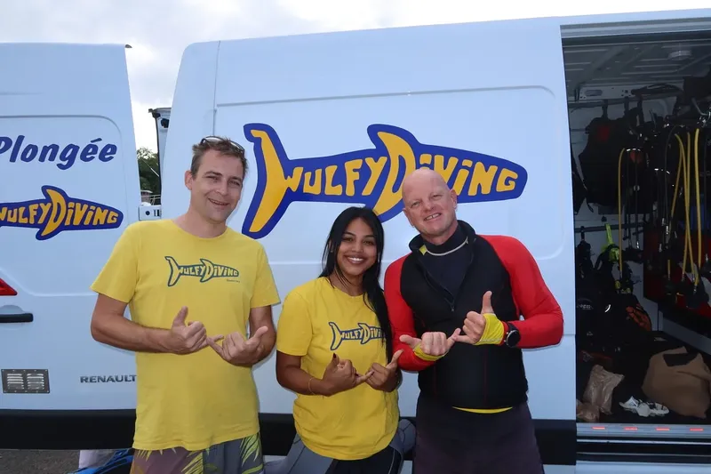 Trois personnes souriantes devant un van de plongée avec logo