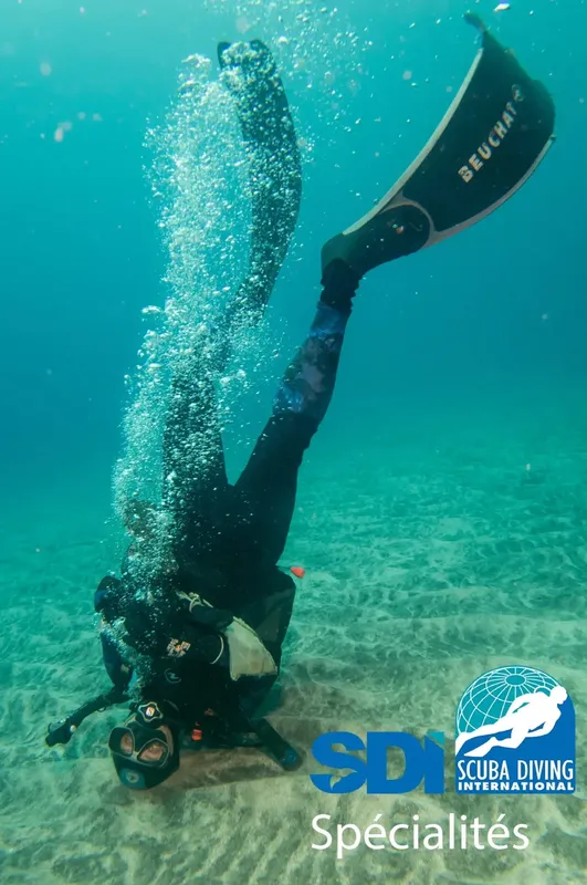 Plongeur en combinaison noire nageant la tête en bas dans l'eau bleue