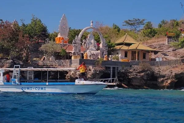 Bateau de plongée amarré devant un temple balinais et des personnes