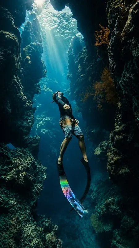 Apnéiste nageant à la verticale dans une grotte sous-marine éclairée