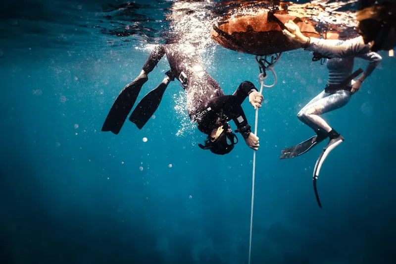 Deux plongeurs en combinaison tirent sur une corde sous l'eau