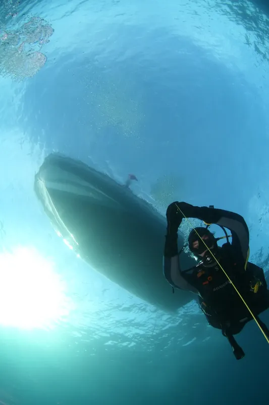 Plongeur en scaphandre regardant un bateau vu d'en bas dans l'eau