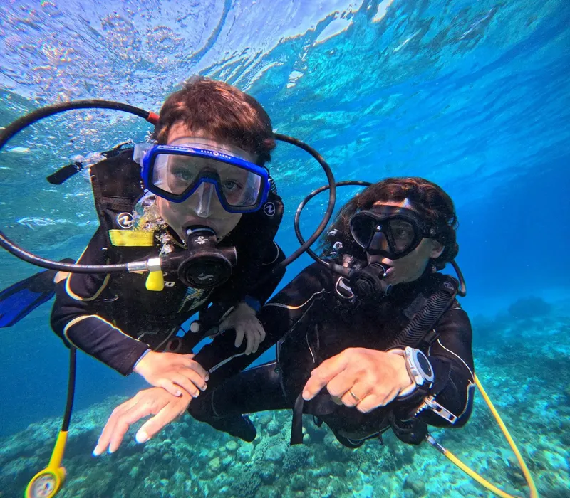 Deux plongeurs souriants regardent la caméra sous l'eau en combinaison