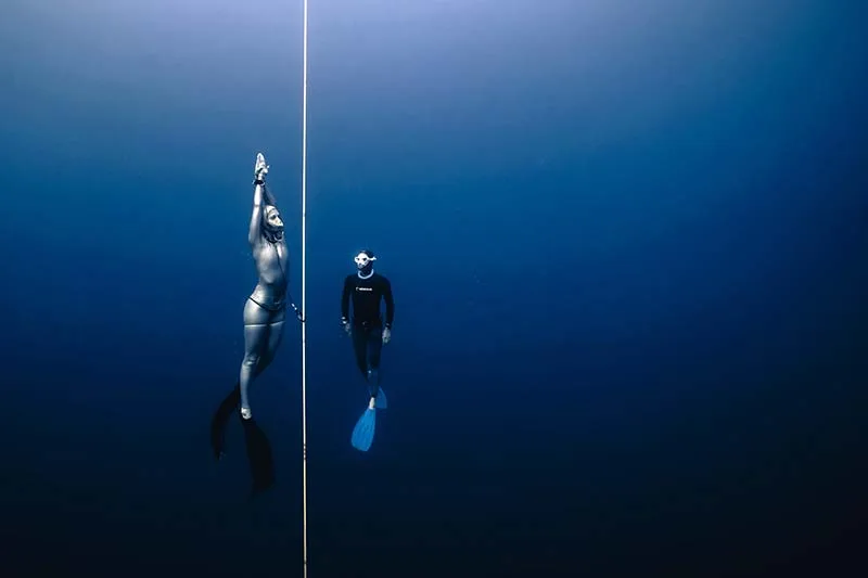 Deux apnéistes évoluent verticalement dans une eau bleue profonde
