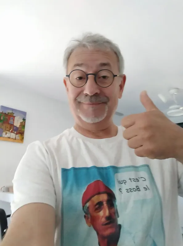 Homme souriant avec lunettes et pouce levé, portant un t-shirt