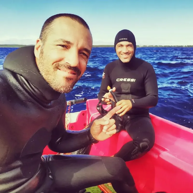 Deux plongeurs souriants en combinaison sur un bateau rouge en mer