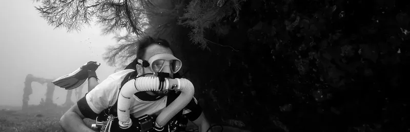 Plongeur en scaphandre regardant vers la caméra dans l'eau sombre