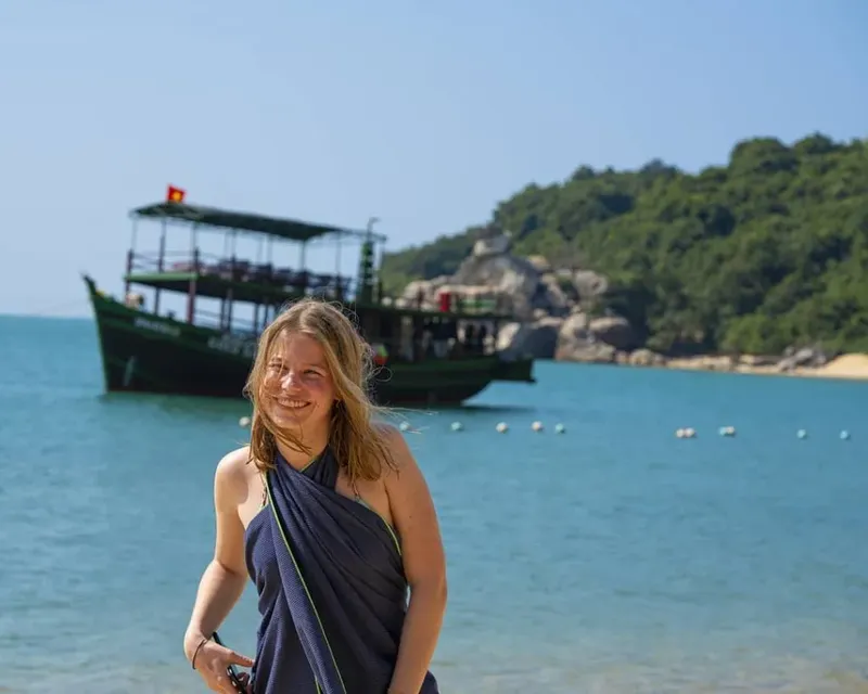 Jeune femme souriante sur une plage avec un bateau en arrière-plan