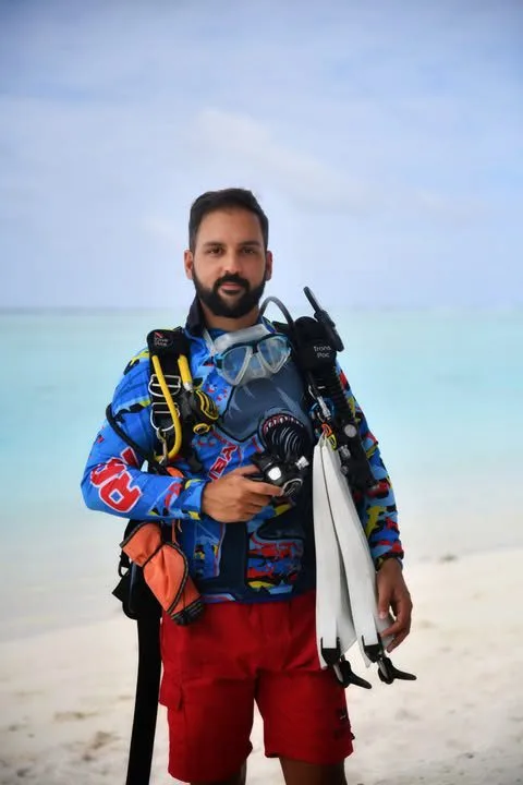 Plongeur souriant sur une plage, équipé de palmes et détendeur