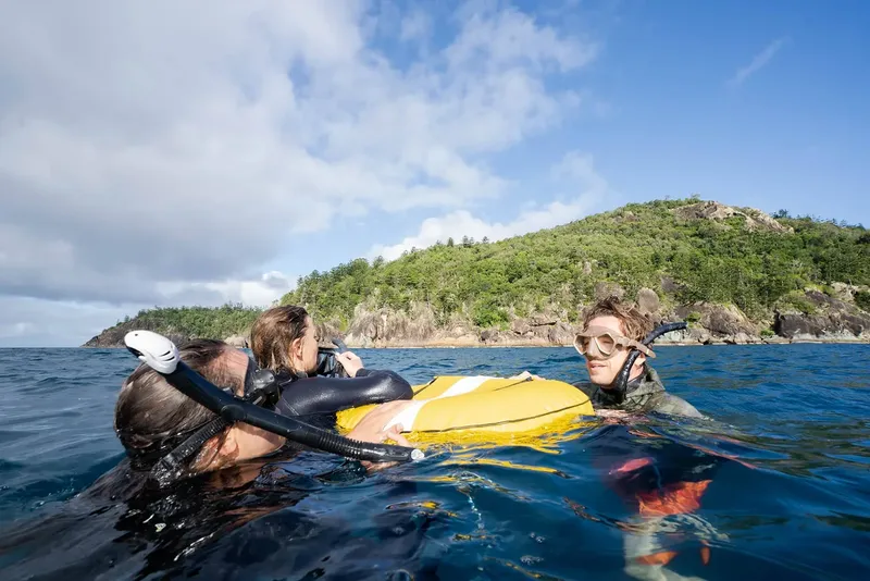 Trois personnes en masque et tuba flottent à la surface de la mer