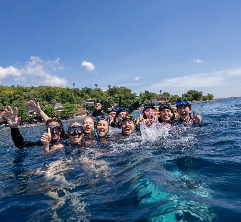 Groupe de plongeurs souriants dans l'eau, paysage tropical en arrière-plan