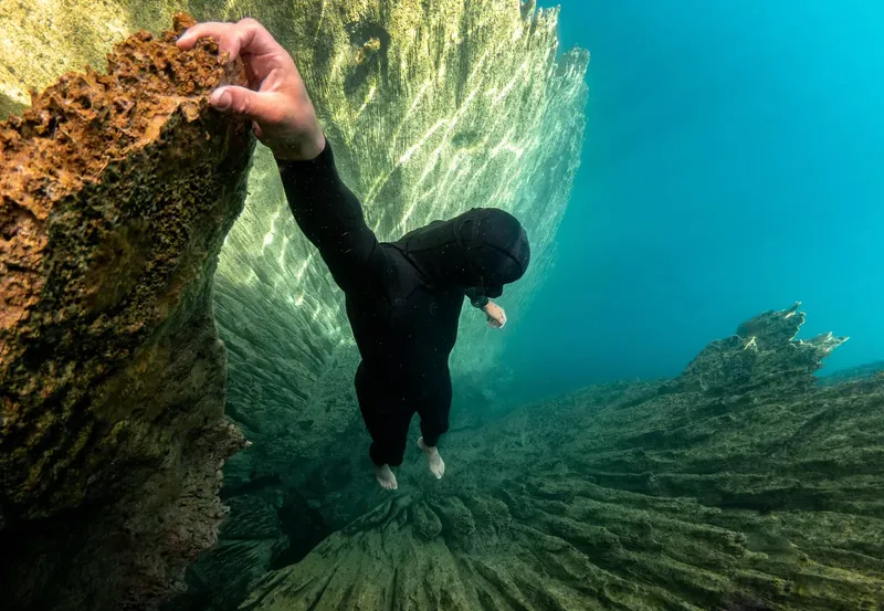 Plongeur en combinaison noire explore une paroi rocheuse sous-marine