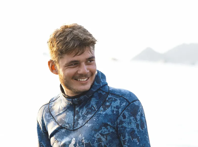 Jeune homme souriant portant une combinaison de plongée près de la mer