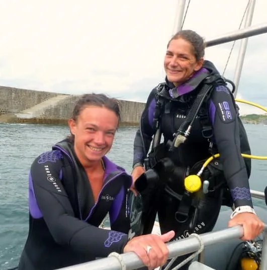 Deux plongeuses souriantes sur un bateau, équipées pour une sortie