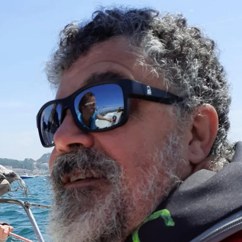 Homme souriant avec lunettes de soleil reflétant un bateau en mer