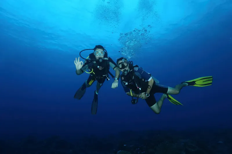 Deux plongeurs souriants nagent ensemble dans une eau bleue claire