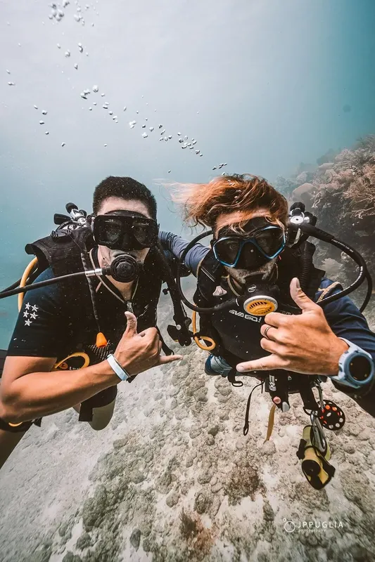 Deux plongeurs souriants font un signe de la main sous l'eau