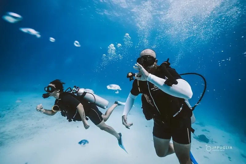Deux plongeurs explorent un fond marin bleu clair avec des bulles