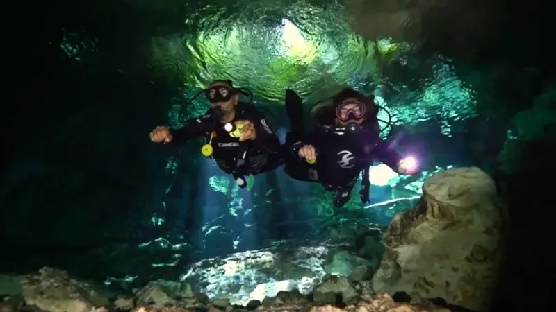 Deux plongeurs explorent une grotte sous-marine éclairée par des rayons de lumière