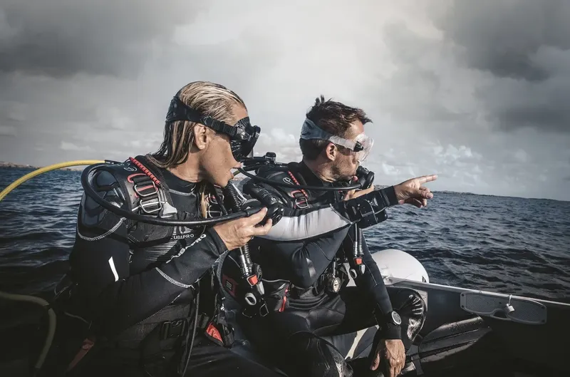 Deux plongeurs en combinaison sur un bateau pointent vers l'horizon