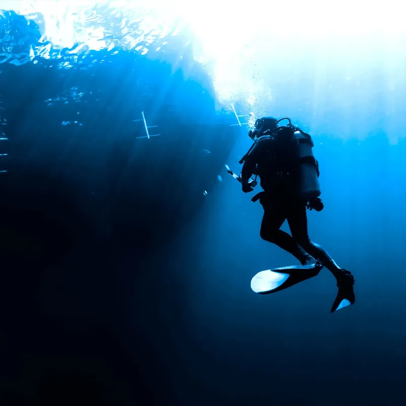 Plongeur évoluant dans une eau bleue, rayons de soleil, silhouette sombre