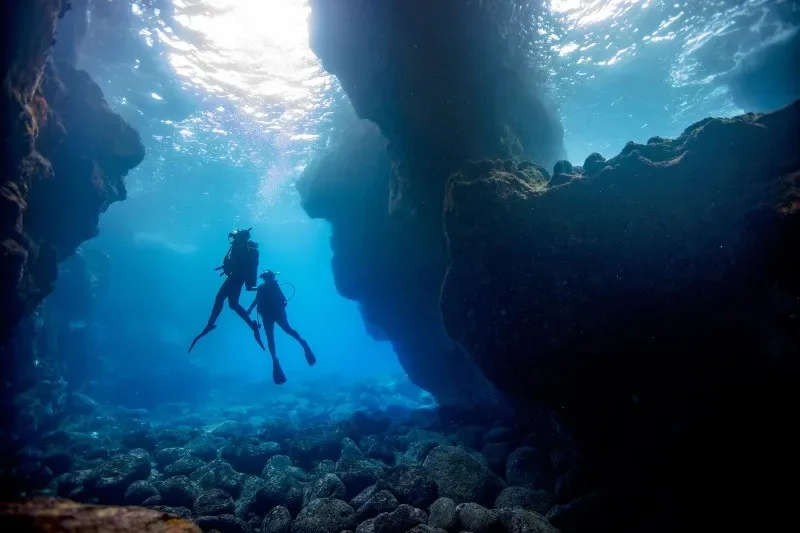 Deux plongeurs explorent une grotte sous-marine éclairée par le soleil