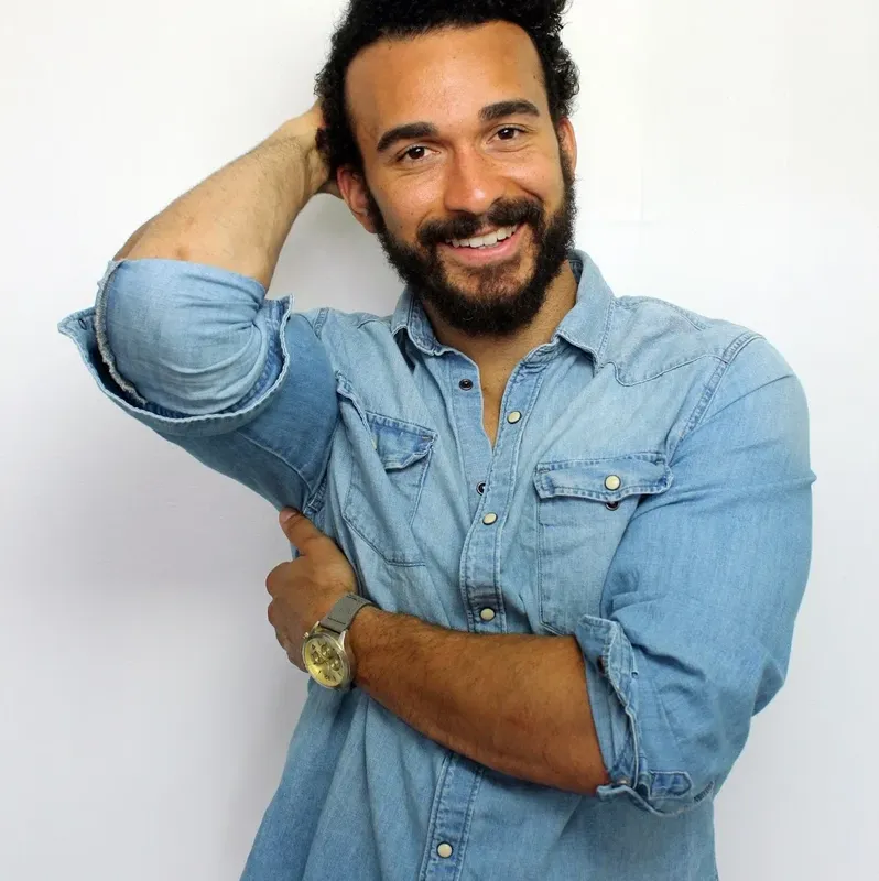 Un homme souriant, barbe fournie, chemise en jean, pose détendue