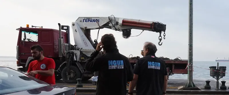 Deux hommes et un autre observent un camion avec une grue près de la mer