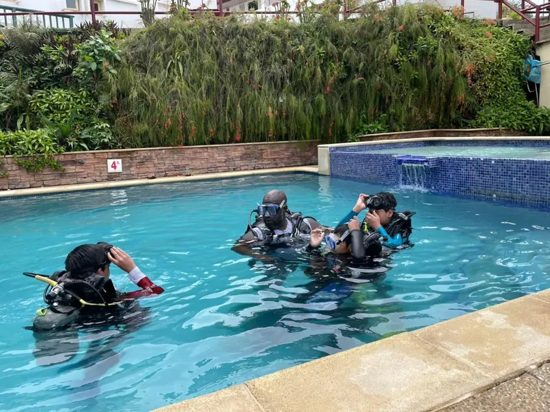 Trois plongeurs en formation dans une piscine, équipement complet visible
