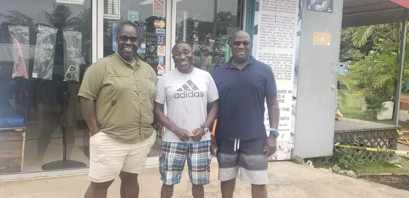 Trois hommes souriants posent devant la devanture d'un centre de plongée