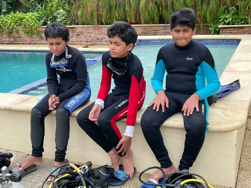 Trois jeunes plongeurs en combinaison près d'une piscine et du matériel
