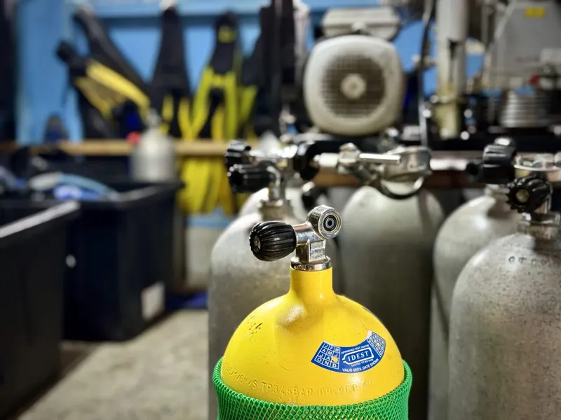 Bouteilles de plongée jaunes avec détendeurs et compresseur en arrière-plan