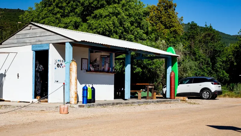 Bâtiment blanc avec bouteilles de plongée, un véhicule et végétation