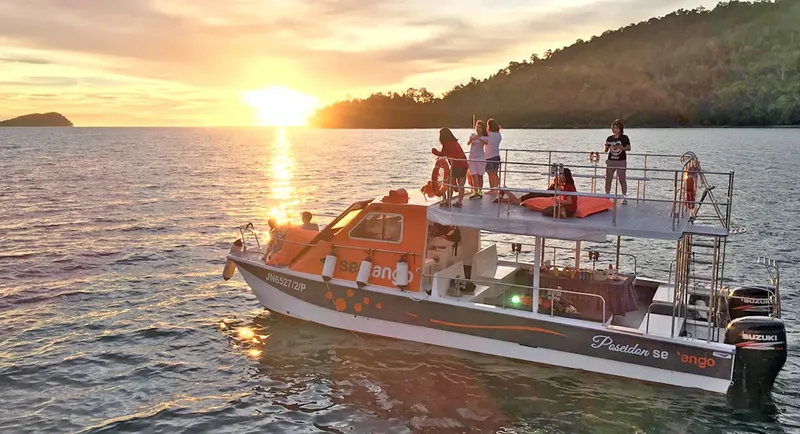 Bateau de plongée orange et blanc avec des personnes au coucher du soleil