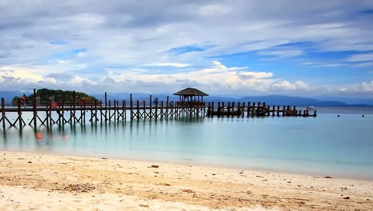 Plage de sable, ponton en bois, mer calme et ciel nuageux