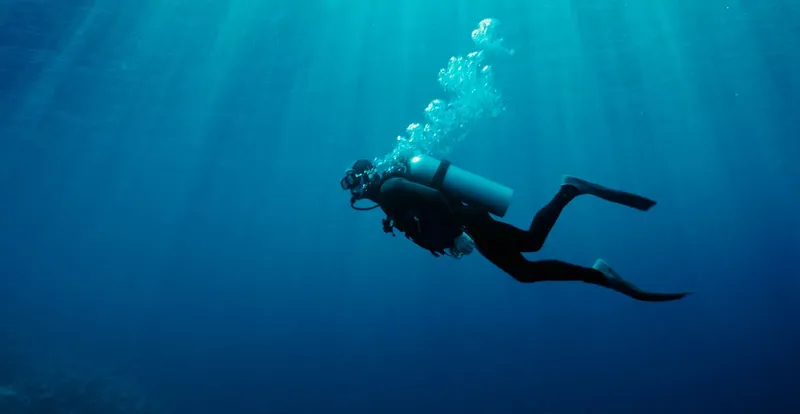 Plongeur en combinaison noire nageant dans une eau bleue claire