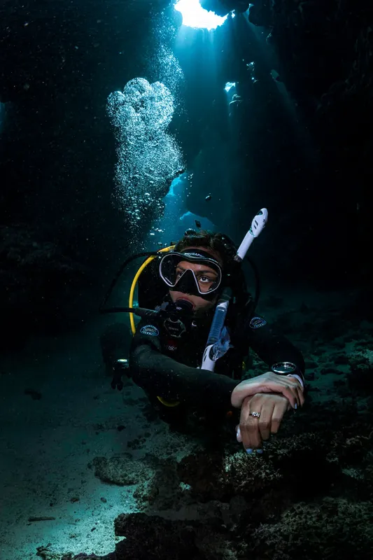 Plongeur en combinaison regarde vers la camera dans une grotte sous-marine