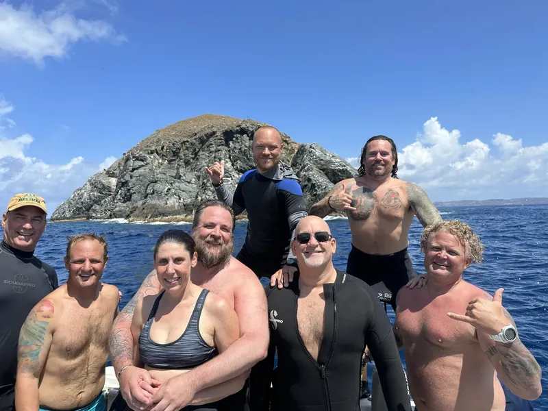 Groupe de plongeurs souriants sur un bateau en mer, île rocheuse