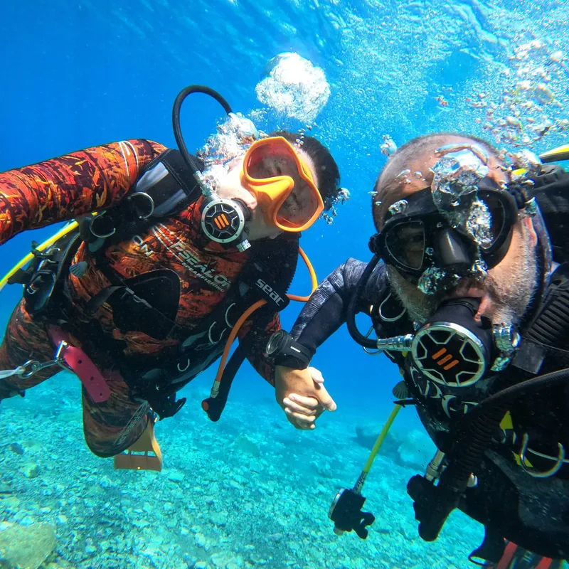 Deux plongeurs se regardent dans l'eau bleue, équipés et souriants